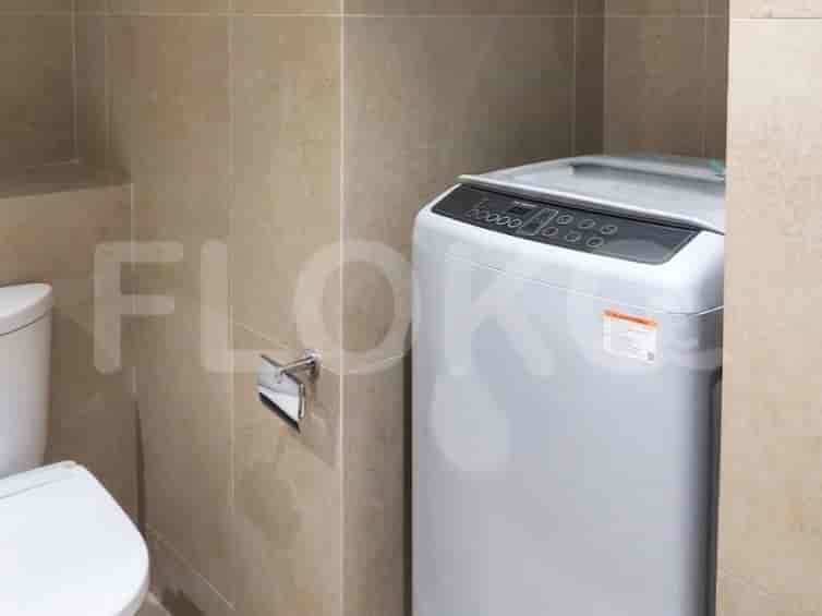 Sudut kamar mandi menampilkan toilet dan mesin cuci.