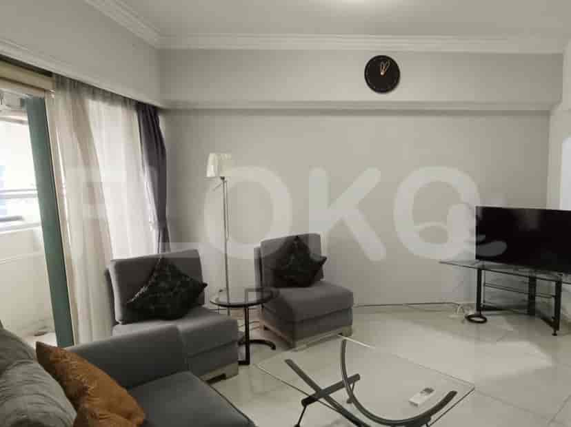 A living room featuring a TV area with a clock and a large window providing natural light.