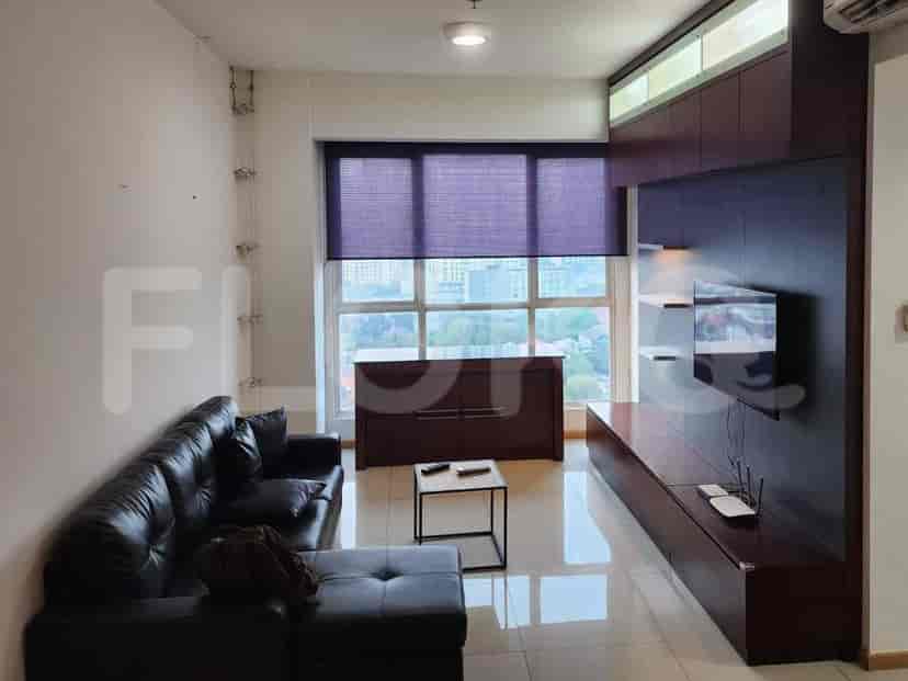 Ruang tamu dengan sofa kulit gelap berbentuk L, unit hiburan besar dengan TV terpasang, dan jendela dengan tirai.