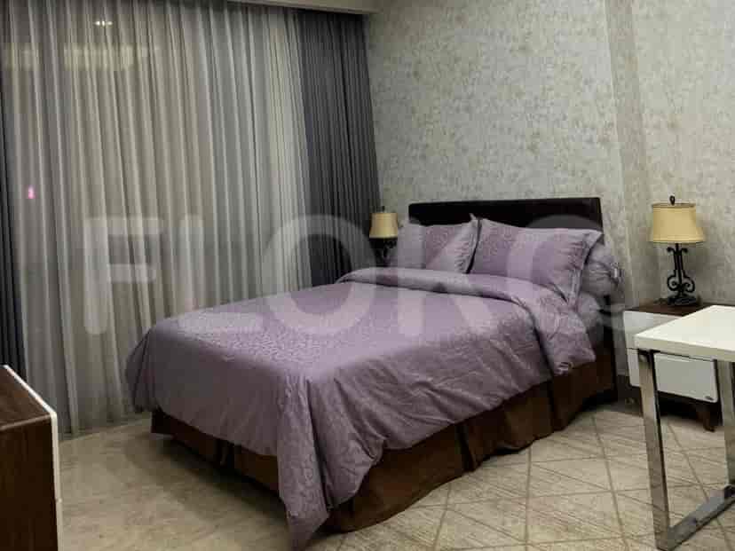 A bedroom featuring a large bed with purple bedding, two bedside lamps, and a view through sheer curtains.