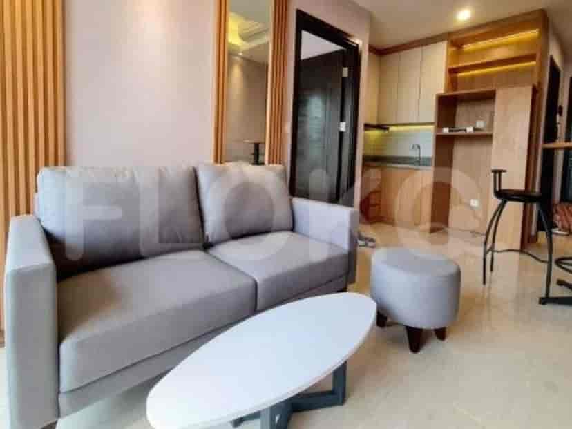 A compact living room featuring a grey sofa, oval coffee table, and a small ottoman, adjacent to a kitchenette.