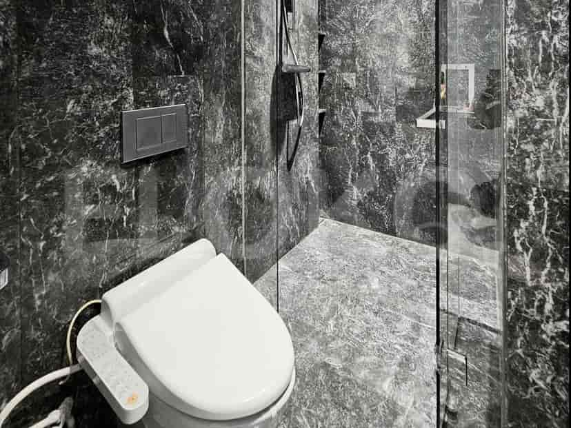 Bathroom with a toilet, glass shower, and marble walls.