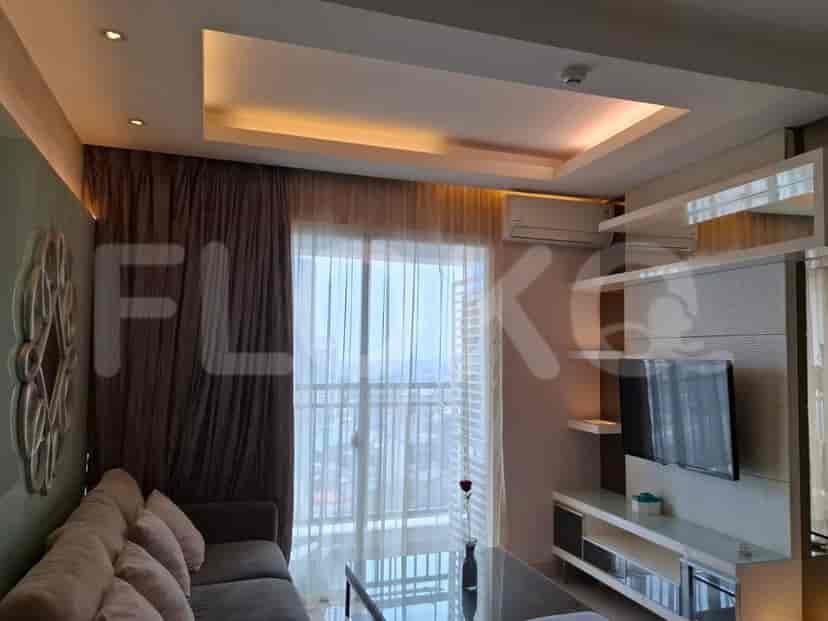 A spacious living room with an L-shaped grey sofa, wall-mounted smart TV, and large window with sheer curtains.