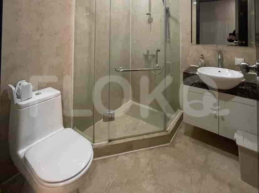 Kamar mandi modern dengan toilet, shower tertutup kaca, dan meja rias dengan bak cuci.