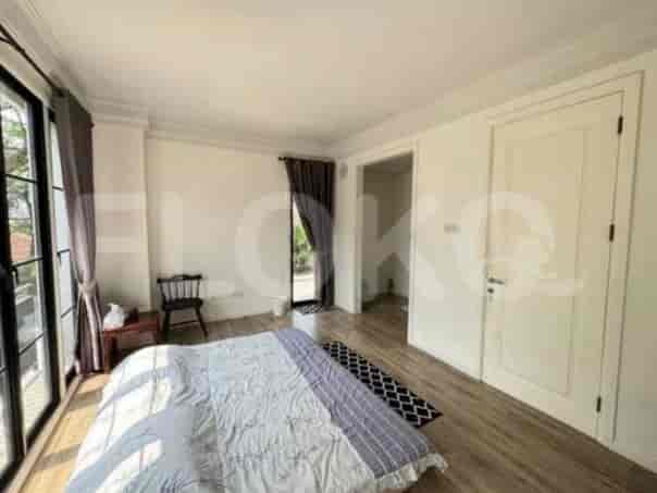 A bedroom with a large bed, wooden flooring, and large windows with dark curtains.