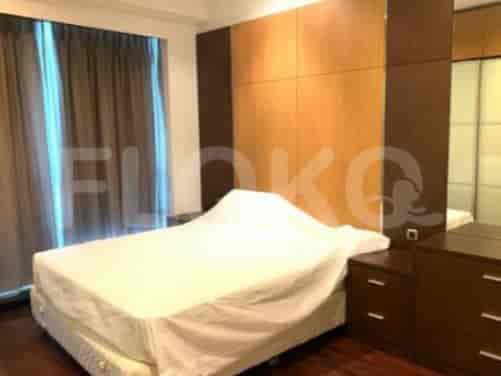 A bedroom with a bed covered by a sheet, a large wooden wall feature, and mirrored closet doors.