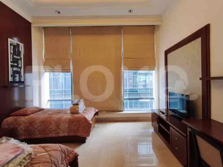 A bedroom with two beds, wooden furniture, and large windows with blinds.