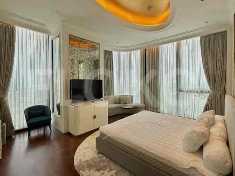A spacious bedroom with a king-size bed, a sitting area with a chair and sofa, and large windows with curtains.