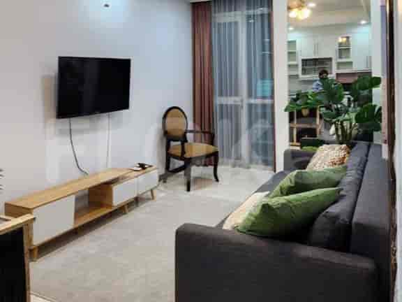 Ruang tamu menampilkan sofa abu-abu gelap dengan bantal hijau, konsol media kayu, dan TV yang terpasang di dinding.