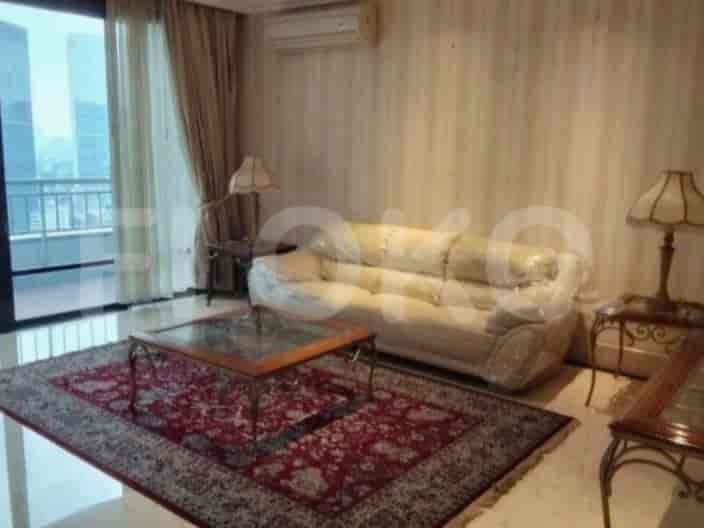 A living room with a sofa covered in plastic, a glass-top coffee table, a patterned rug, and a lamp.