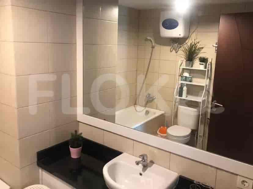 Kamar mandi dengan dinding ubin krem, wastafel, toilet, dan bak mandi dengan pancuran.