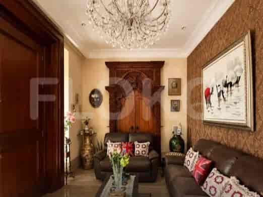 Ruang tamu mewah menampilkan dua sofa kulit coklat, ukiran kayu berukir besar, dan lampu gantung kristal.