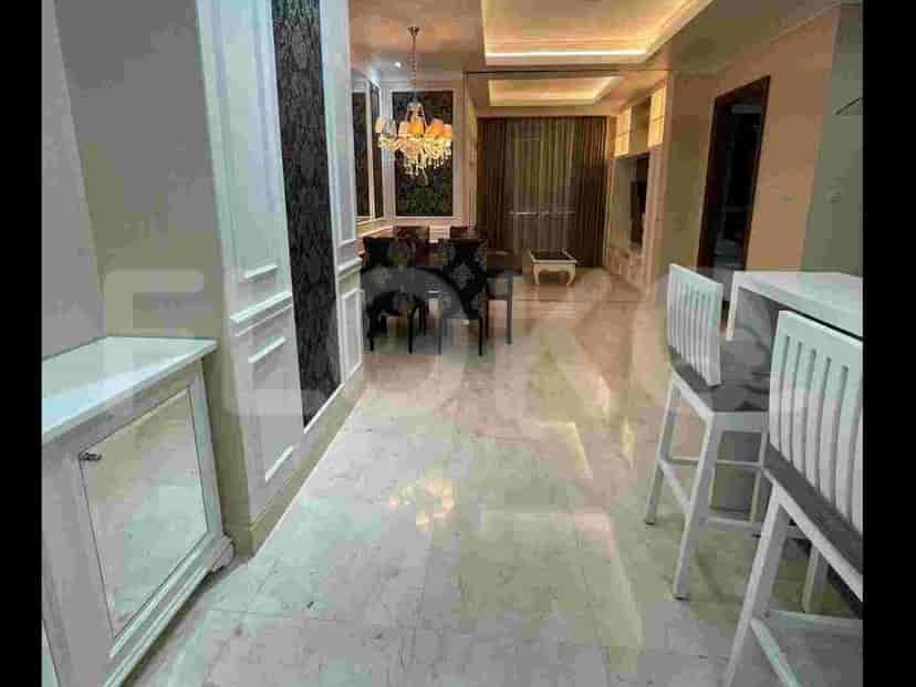 A kitchen island with white bar stools and a white countertop, adjacent to a marble-floored hallway.