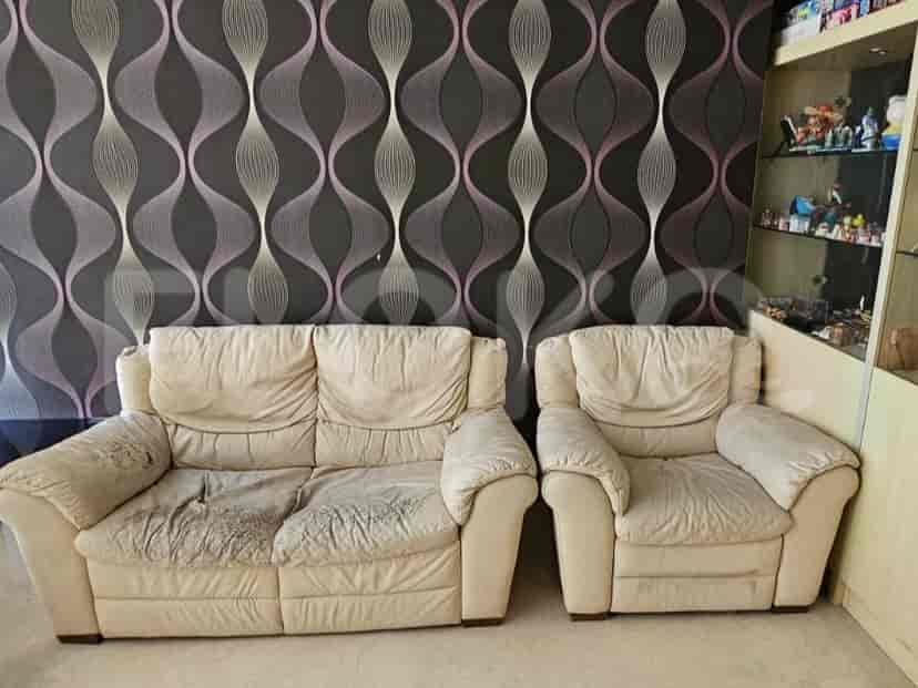 A living room with a worn beige sofa and armchair against a dark patterned wallpaper.