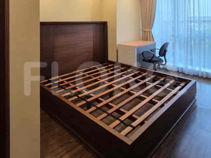 A bedroom with a large wooden bed frame, a small desk, and a chair near a window with curtains.
