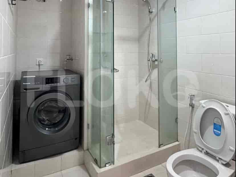 A modern bathroom with a washing machine, a glass-enclosed shower, and a toilet.