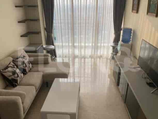 The living area features a grey L-shaped sofa, a wall-mounted TV, and a large window.
