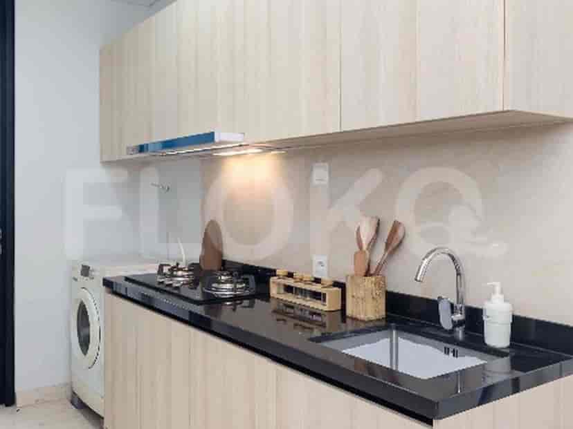 A compact kitchen with light wood cabinets, a black countertop, a sink, and a gas stove.