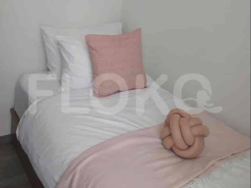 A close-up of a single bed with white bedding, a pink throw blanket, and a knot pillow.