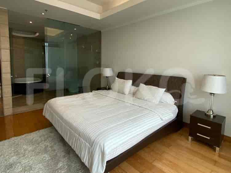 Kamar tidur utama dengan tempat tidur, meja nakas, lampu, dan pemandangan ke kamar mandi dalam dengan bak mandi.