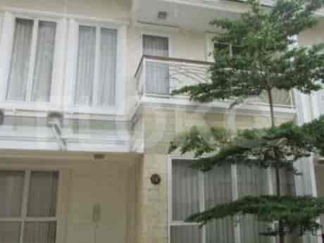 Sebuah rumah dua lantai dengan balkon, jendela besar, dan pohon kecil di depannya.
