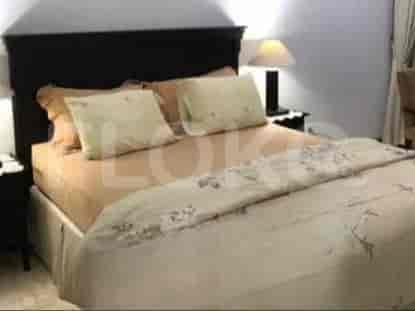 Kamar tidur menampilkan tempat tidur besar dengan seprai krem dan meja nakas kayu.