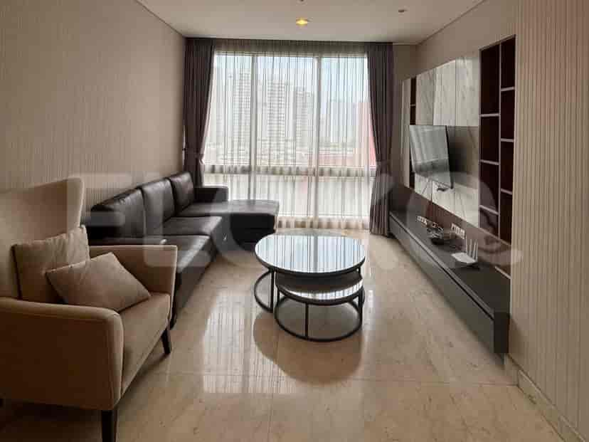 A modern living room featuring a sectional sofa, coffee table, TV console, and a large window with city views.