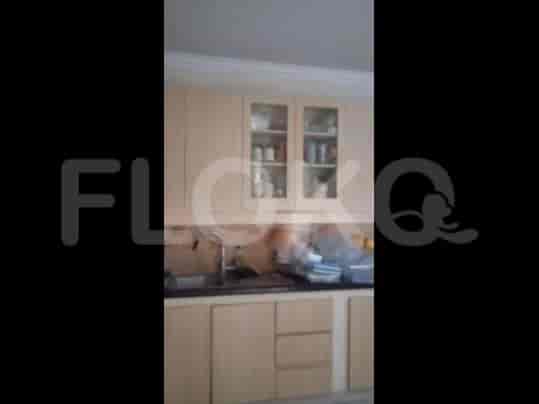A kitchen with light-colored wooden cabinets, glass-fronted upper cabinets, and a stainless steel sink.