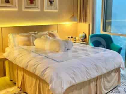 A bedroom with a large bed, bedside tables, a globe, and a green armchair near a window.