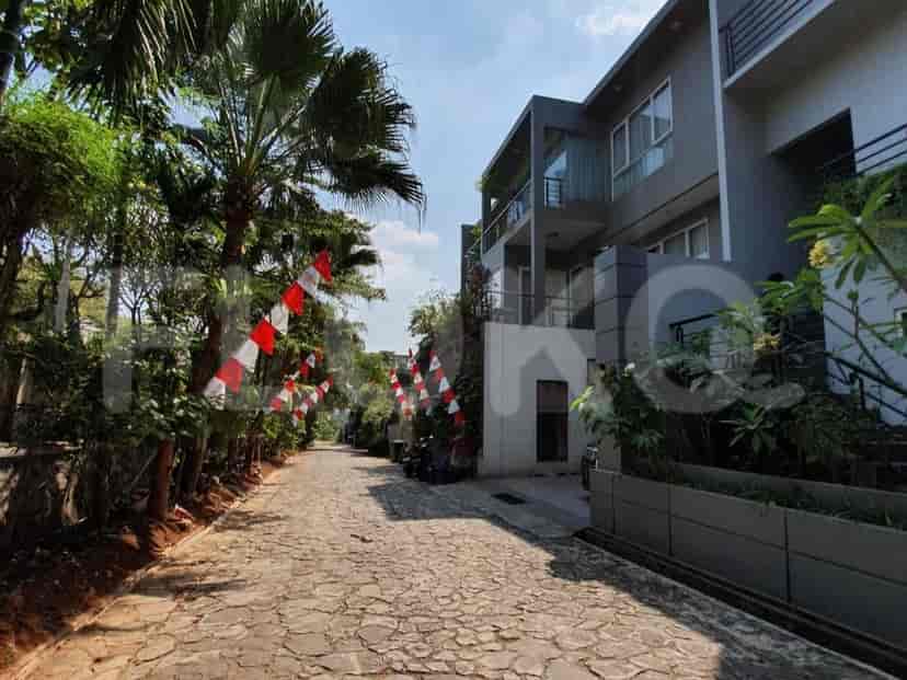 Jalan batu bulat yang diapit oleh pohon palem dan bendera Indonesia merah putih, mengarah ke deretan townhouse abu-abu modern.