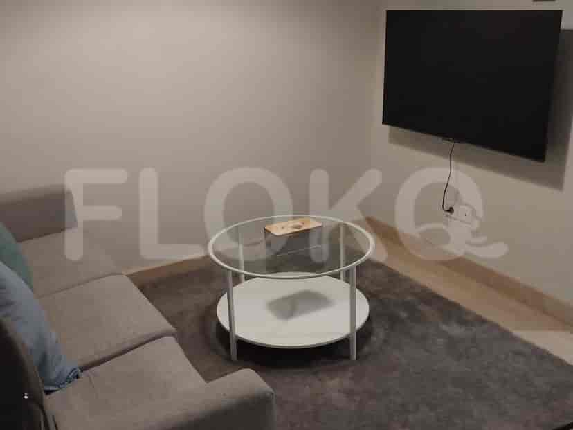 A living room featuring a grey sofa, a round glass coffee table, a wall-mounted TV, and a dark grey carpet.