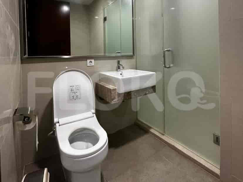 Sebuah kamar mandi modern dengan toilet terpasang di dinding, wastafel di atas meja, dan pancuran berlapis kaca.