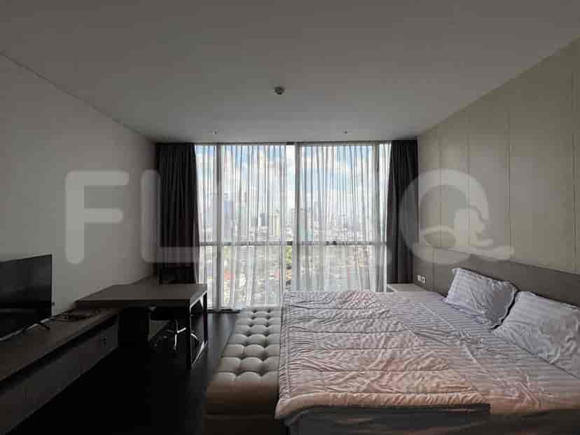 A bedroom with a queen-size bed, a desk, a TV, and large windows offering a city view.