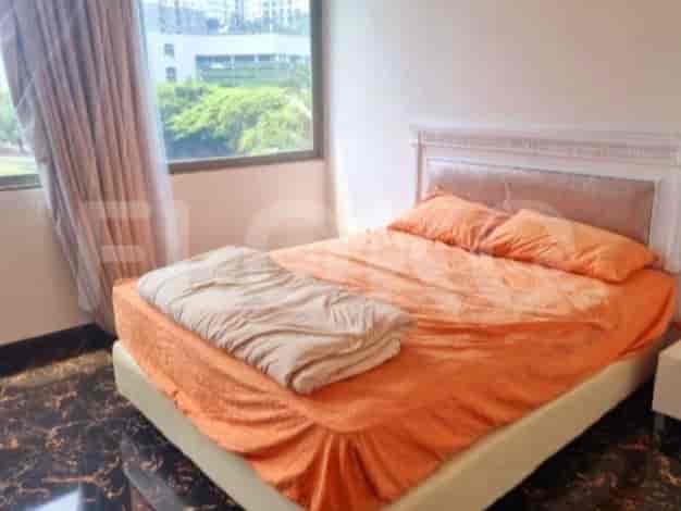 A bedroom with a queen-sized bed, orange bedding, and a large window with curtains.