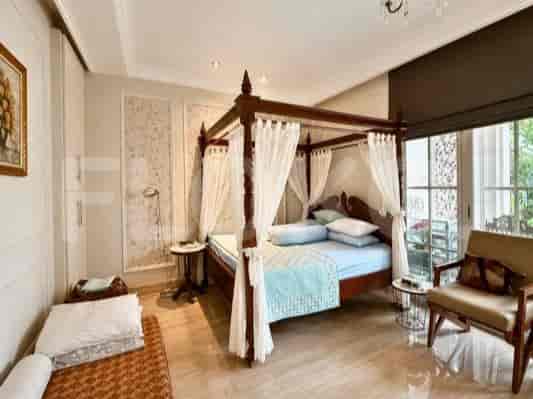 Kamar tidur dengan tempat tidur berkanopi yang ditutupi tirai tipis putih, kursi berlengan kayu, dan sofa tempat tidur.