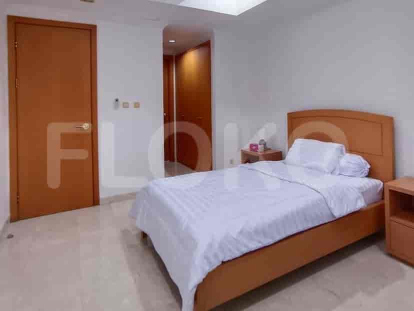 A bedroom with a wooden framed bed with white striped bedding, a wooden bedside table, and a wooden door.
