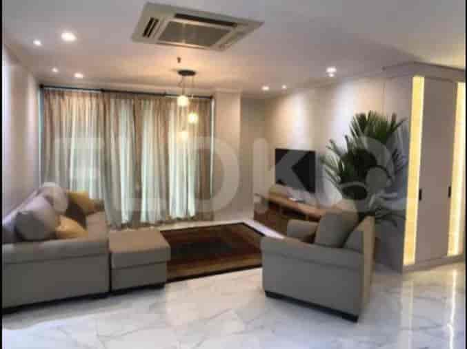 A spacious living room with an L-shaped grey sofa, wall-mounted smart TV, and large window with sheer curtains.