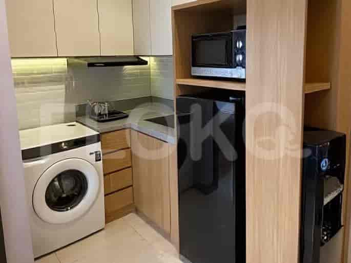 A compact kitchenette with a washing machine, microwave, refrigerator, and wooden cabinetry.