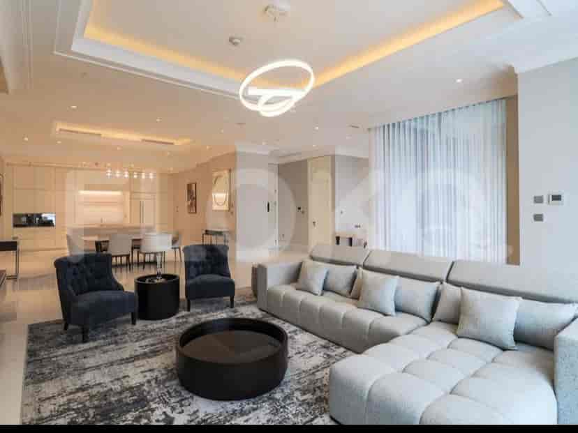 A spacious living room with an L-shaped grey sofa, wall-mounted smart TV, and large window with sheer curtains.