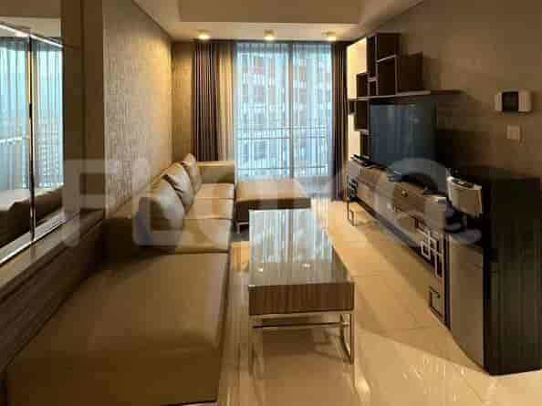 Sebuah ruang tamu modern dengan sofa sectional besar berbentuk L, meja kopi kaca, konsol TV dengan TV yang terpasang di dinding, dan jendela dari lantai ke langit-langit.