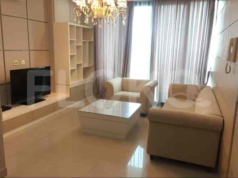 Sebuah ruang tamu dengan set sofa krem, meja kopi putih, TV yang terpasang di dinding, dan rak buku.
