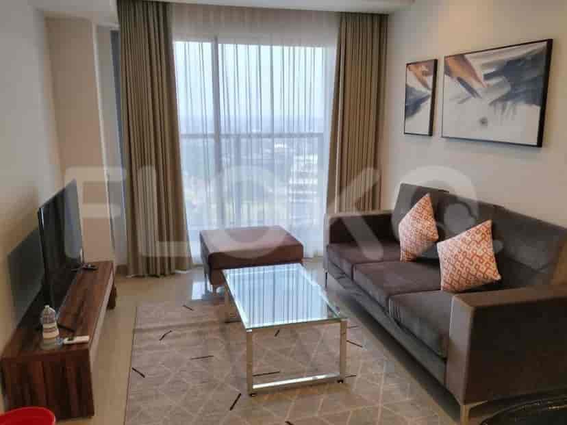 Sebuah ruang tamu dengan sofa abu-abu gelap, meja kopi kaca, ottoman, dan meja TV dengan TV.