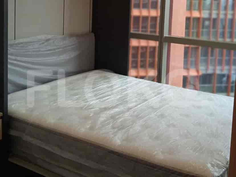 A bedroom with a bed covered in protective plastic, adjacent to a window with a city view.