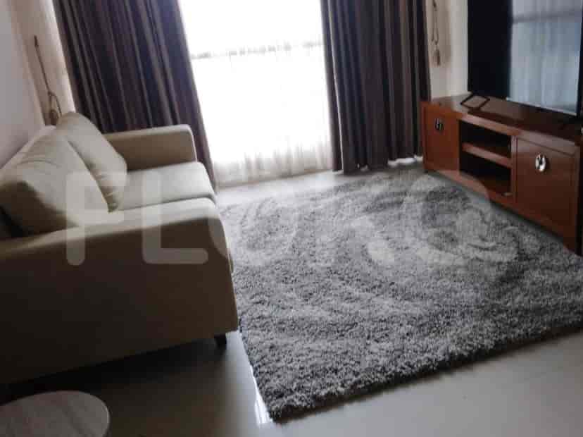 Ruang tamu dengan sofa abu-abu, TV, dan jendela besar.