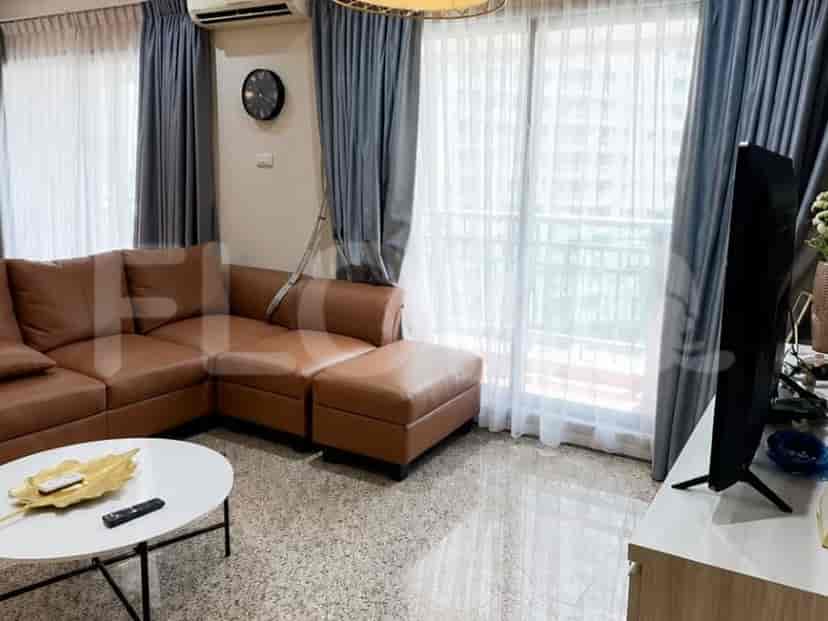 A cozy living room featuring a brown sectional sofa, a white coffee table, a wall clock, and a large window with dual curtains.
