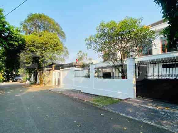 A view of the house from the street, showing a white wall, black metal gate, and lush trees.