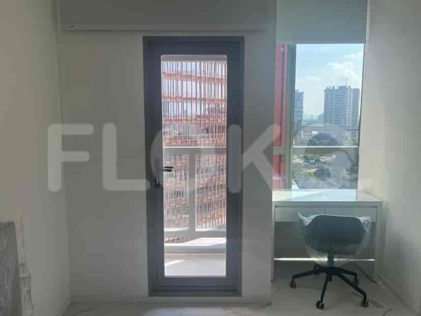 A room with a desk, chair, door leading to a balcony, and a large window with a city view.