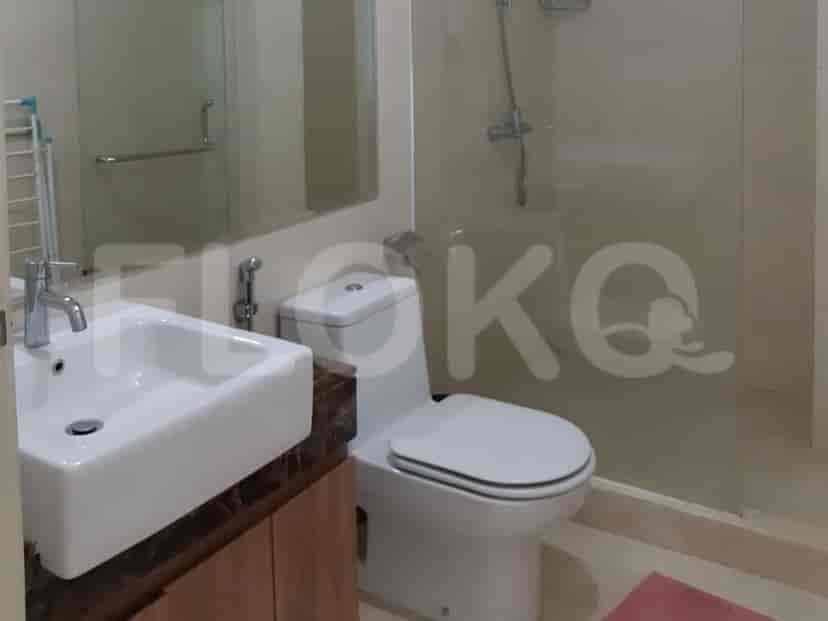Kamar mandi modern dengan wastafel putih, toilet, dan pancuran tertutup kaca.