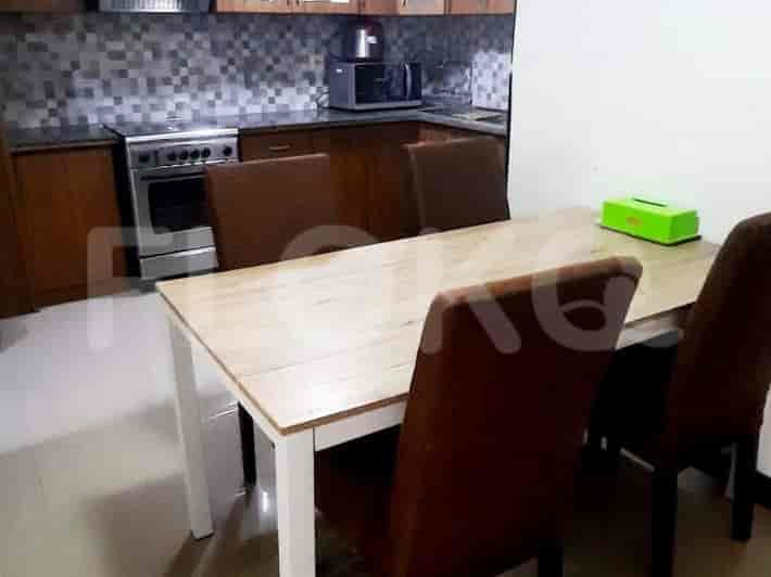 A dining area with a wooden table, chairs, and a kitchen with appliances in the background.