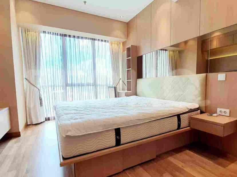 A bedroom with a large bed, bedside table, and a window with sheer curtains.